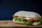 Tasty panini burger with bacon, cheese, salad and chicken meat on a wood platform on a blue paper background. Tasty