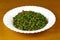 Tasty Peas with ham on a white plate and wooden background. Close up view