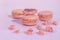 Tasty pink raspberry macarons on light violet background. French homemade dessert with small broken pieces