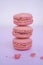 Tasty pink raspberry macarons on light violet background. French homemade dessert with small broken pieces