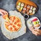 Tasty Pizza with salami, set of sushi rolls and hands take food. Dark background. Flat lay, top view.