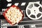 Tasty popcorn in paper package and film reel on clapperboard, top view