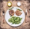 Tasty pork steak with green salad, oil and salt, a knife and fork wooden rustic background top view close up