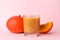 Tasty pumpkin juice in glass, whole and cut pumpkins on pale pink background