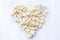 Tasty salted popcorn in shape of heart on white background.