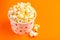 Tasty salty popcorn in paper cup on bright orange background