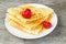 Tasty sweet thin pancakes with fresh strawberries and honey on plate, delicious dessert, closeup, wooden background