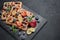 Tasty waffles with berries, mint and sweet sauce on slate serving board on grey background. Top view. Sweet meal. Dessert