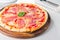Tasty whole Italian pizza topped with thinly sliced prosciutto ham on the served restaurant table.