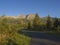 Tatra Mountains range with asphalt road curve, golden hour light, way from Tatranska Lomnice to Start with green trees and grass.