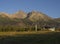 Tatra Mountains range gold colored sunrise light , ski lift at Tatranska Lomnice with green trees and grass. Early autumn panorama