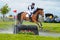 Tattersalls horse show in Ireland, chestnut horse jumping over obstacle in water with male rider, jockey rushing forward