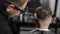 Tattoed barber makes haircut for customer at the barber shop by using hairclipper, man`s haircut and shaving at the