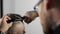 Tattoed barber makes haircut for customer at the barber shop by using scissors and comb , man`s haircut and shaving at