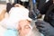 Tattoo artist holds the client`s eyebrow with her hand, thereby stretching the skin and performing permanent makeup with a