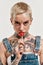 Tattoo and piercing. A white pierced and tattooed woman wearing a denim overall sucking a lollipop while looking into a