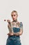 Tattoo and piercing. A white pierced woman with tattoos wearing a denim overall holding a lollipop and looking sideways