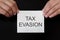 Tax evasion mug shot concept. Criminal hands holding paper placard with written word in dark black background.