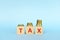 Tax word on wooden blocks in blue background with increasing stack of coins. Rising tax concept.