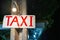 Taxi sign on white wood, artisanal and sloppy hangs on a concrete pole on a night street in Asia, Thailand. sanctified by a dim