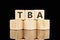 TBA text assembled from wooden cubes on a black background