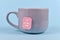 Tea bag with made up cute pink label with text `Get well soon` in gray cup on blue background