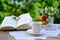 Tea, coffee in white mug on saucer, open book, fruits, lace napkin, bouquet of wild flowers on wooden table in garden, blurred