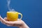 A tea cup made of lemon. Lemon cup in hand on a blue background. Creative composition on theme of natural fruit tea