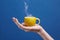 A tea cup made of lemon. Lemon cup in hand on a blue background. Creative composition on theme of natural fruit tea