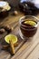 Tea in glass teacup with lemon. Near glass teapot, cinnamon sticks, jam in jar, hazelnuts and lemon at wood background
