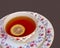 Tea party.  Black tea with a round slice of lemon in an ornamental porcelain cup with saucers on a textured textile background