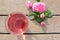 Tea rose herbal tea in a glass cup with pink buds and flowers on a rustic wooden table. Summer tea party outdoors