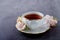 Tea time backdrop with vintage white porcelain tea cup, gentle pink roses on a dark gray background