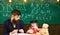 Teacher with beard, father teaches little son in classroom, chalkboard on background. Boy, child on calm face holds