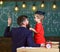 Teacher with beard, father teaches little son in classroom, chalkboard on background. Instructive conversation concept