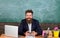 Teacher bearded hipster with eyeglasses sit in classroom chalkboard background. Teacher sit at desk with laptop. Back to