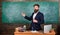 Teacher bearded man tell interesting story. Teacher charismatic hipster stand near table classroom chalkboard background