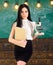 Teacher of biology holds book and microscope. Biology concept. Lady in formal wear on calm face in classroom. Lady