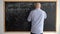 The teacher at the blackboard is a man of 40s without a face, writing down mathematical formulas with chalk. Online math