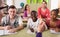 Teacher calls student at far desk to answer. Focus on girl on right above