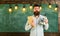 Teacher in eyeglasses holds book and microscope. Man with beard and mustache on surprised face in classroom. Scientific