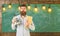 Teacher in eyeglasses holds book and microscope. Man with beard and mustache on surprised face in classroom. Scientific