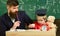 Teacher in formal wear and pupil in mortarboard in classroom, chalkboard on background. Father checking hometask, helps