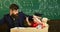 Teacher in formal wear and pupil in mortarboard in classroom, chalkboard on background. Father teaches son mathematics