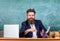 Teacher formal wear sit table classroom chalkboard background. Pay attention to details. Teacher concentrated bearded