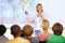Teacher, geography and map in classroom with children, pointing and smile with test question. Person, teaching and