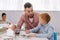 teacher helping little boy to draw picture at table