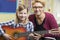 Teacher Helping Pupil To Play Guitar In Music Lesson