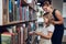 Teacher helping to choose book her schoolgirl in school library. Smart girl selecting literature for reading. Books on shelves in