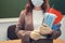 A teacher holds medical masks and a sanitizer in a school classroom